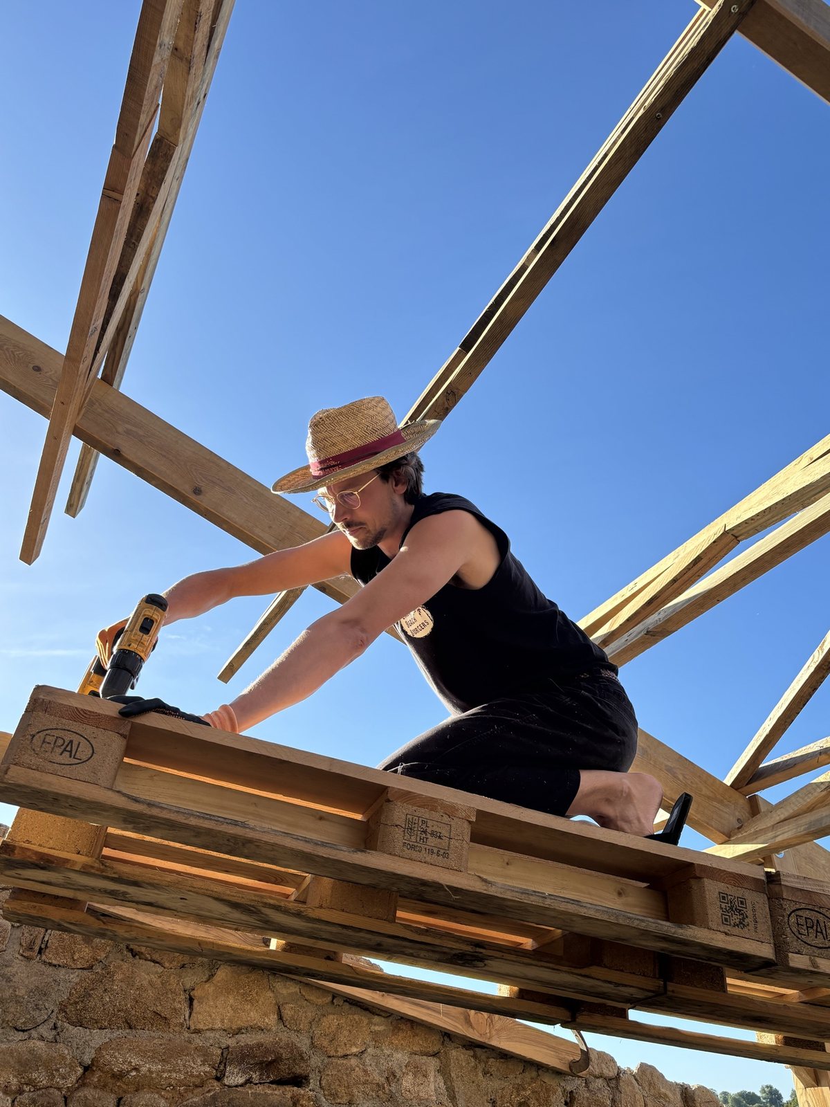 Thijs drilling pallets into the roof frame of the farmhouse at Project Q