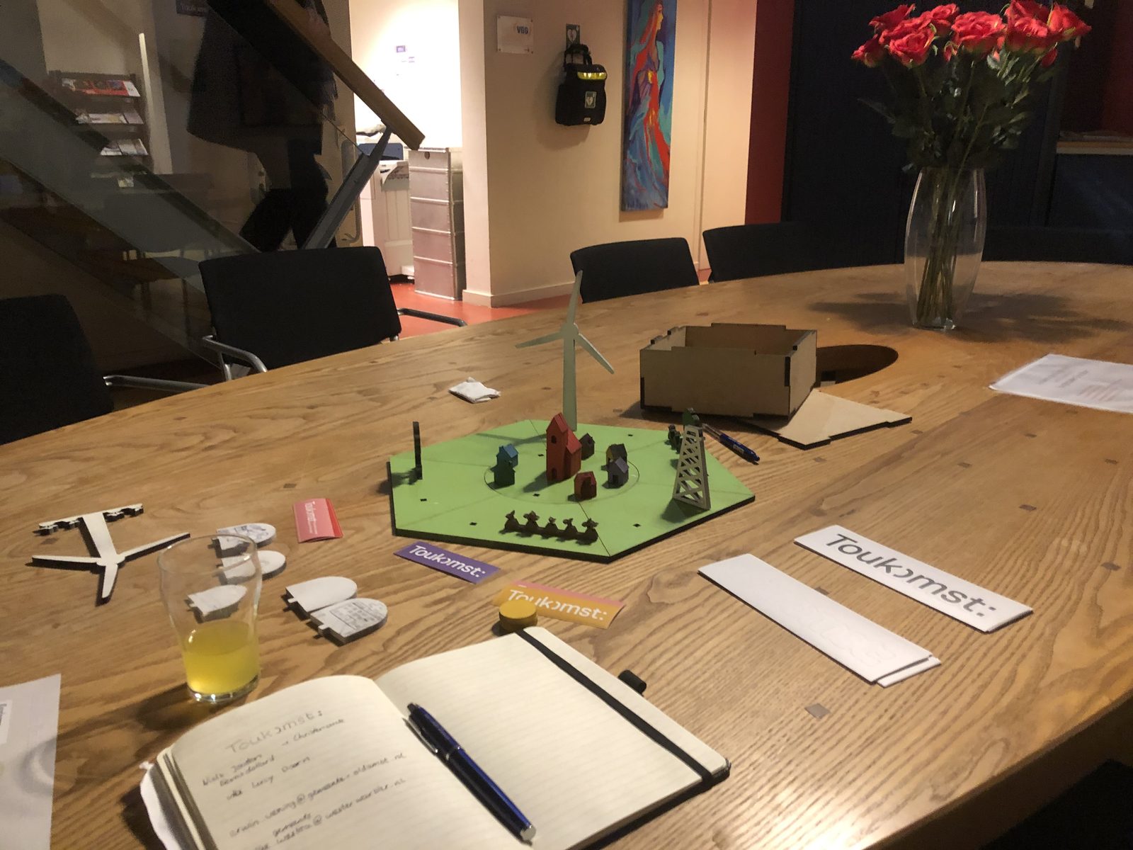 The Toukomst serious game set up on a table, with a model village, game pieces and notebooks